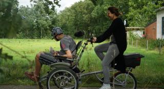 Een cliënt en begeleider fietsen met een rolstoelfiets.